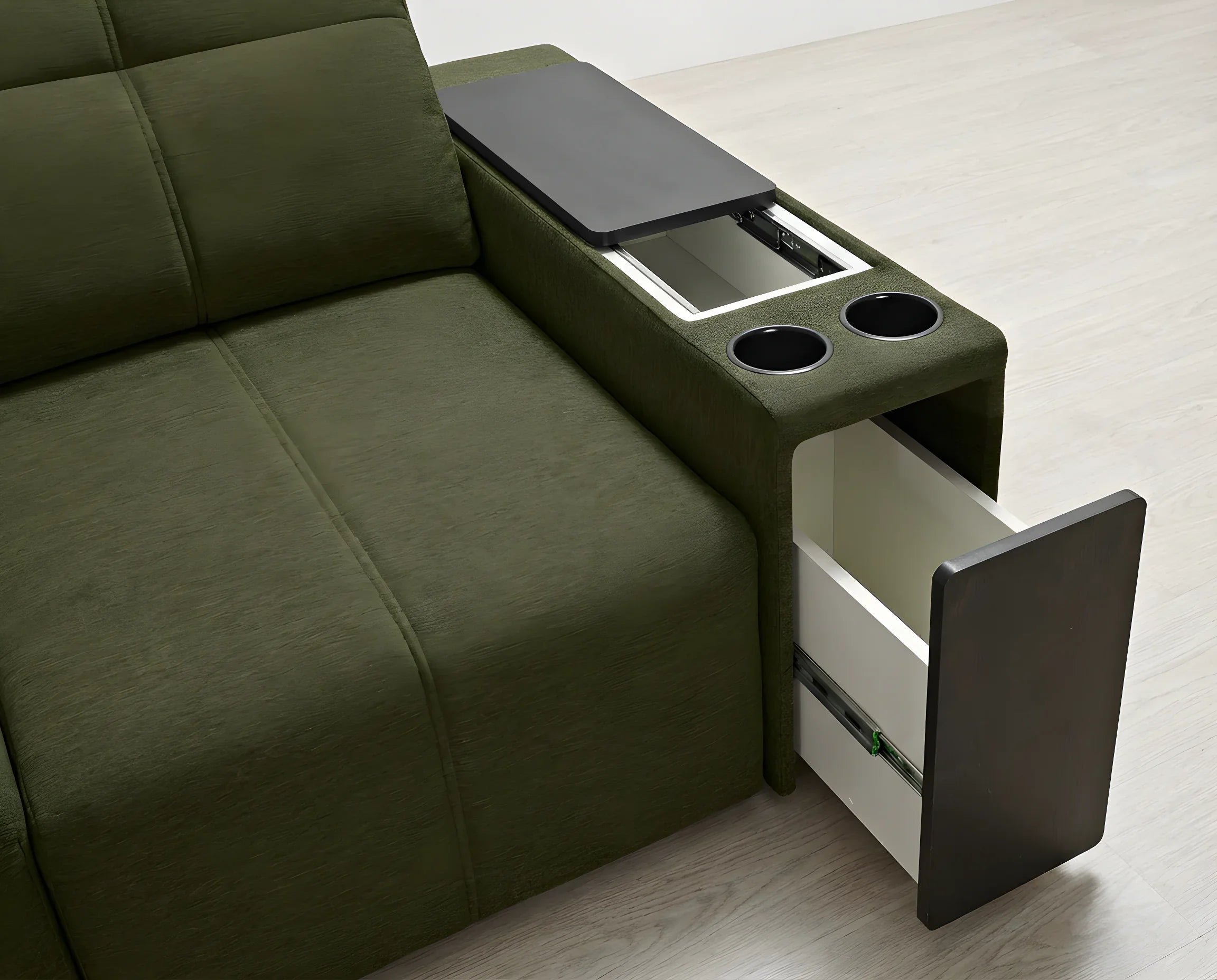 Canapé vert en tissu avec accoudoir, table encastrée, deux porte-gobelets et tiroir ouvert, sur parquet clair